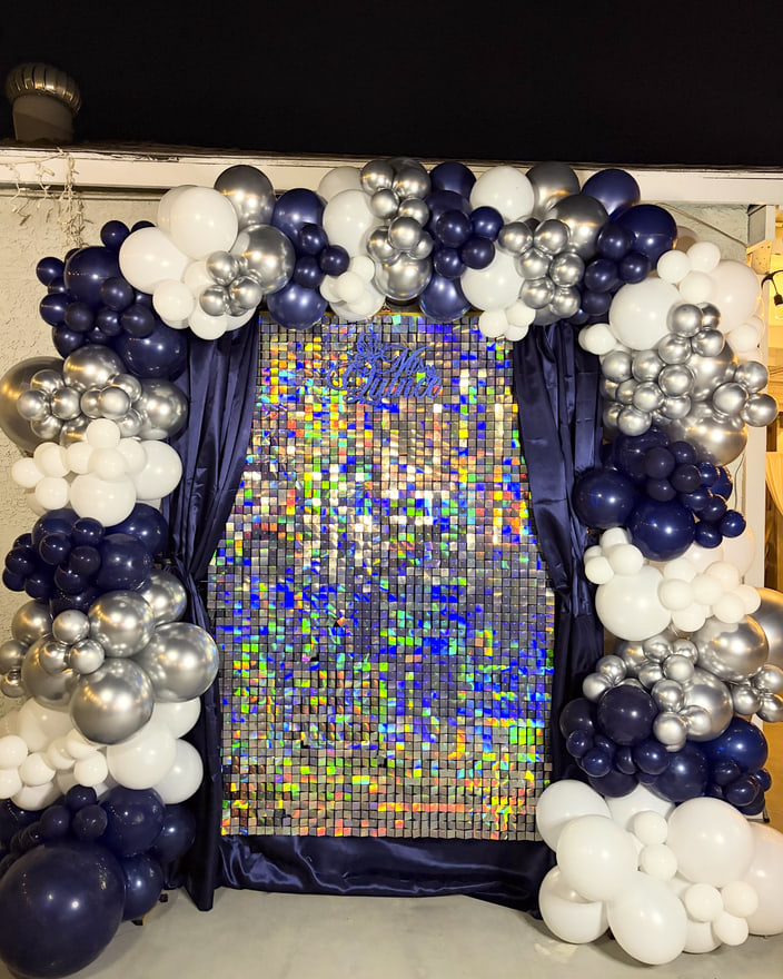 A silver sequin shimmer wall framed by a balloon garland in navy, silver and white.