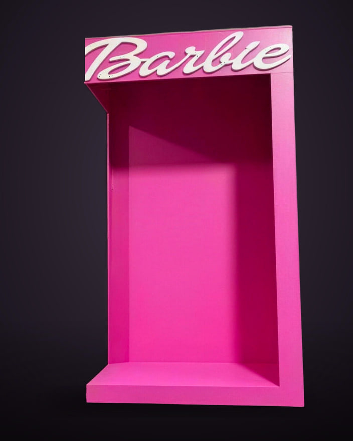 A life-size pink doll-box photo op, empty, standing against a studio backdrop.