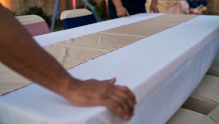 Hands smoothing a white linen along a long trestle table