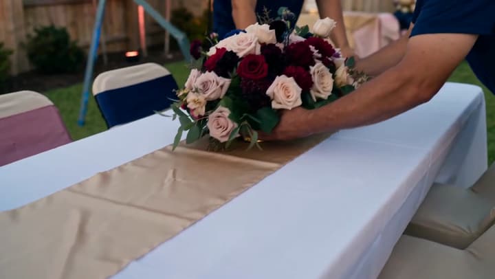 A floral centrepiece being set down on a dressed table